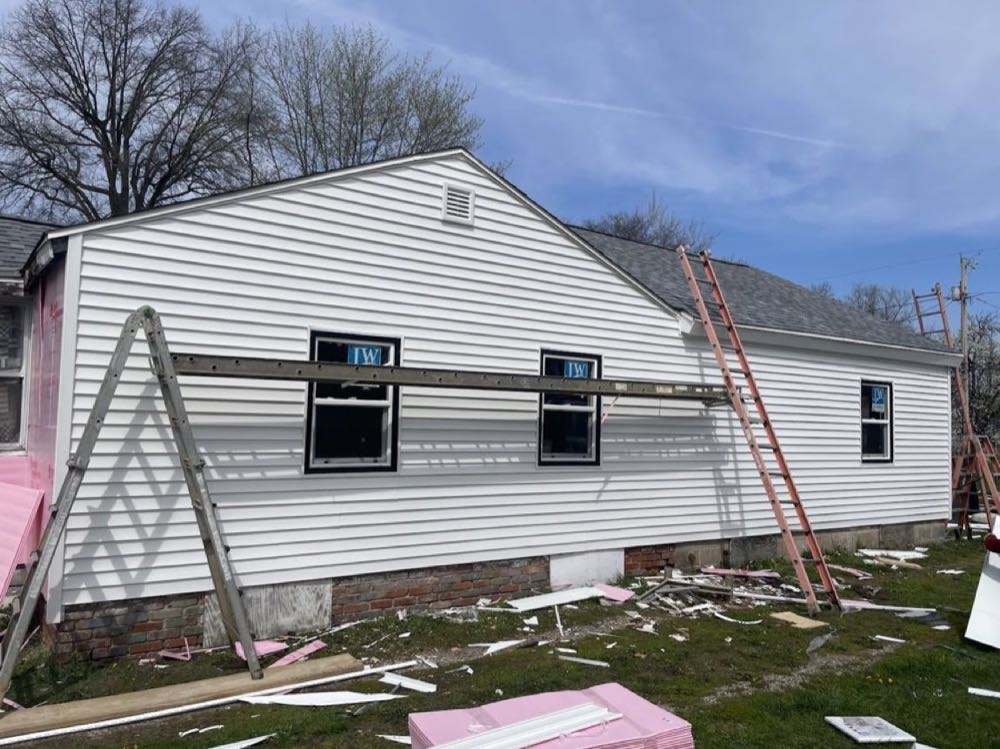 Crew mid-job replacing siding on a house, ladders up and new panels going on