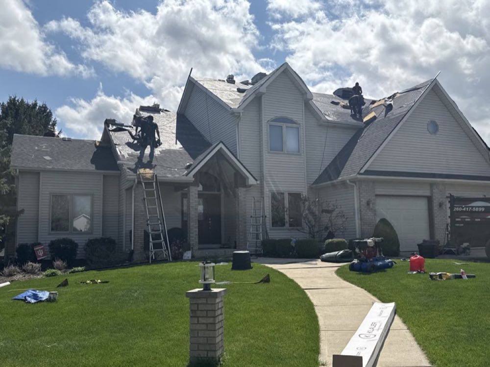 Crew on a two-story roof mid tear-off with the branded truck in the driveway